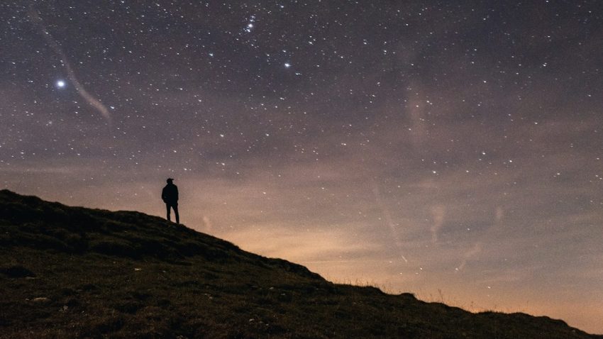 a person standing on a hill with a starry sky above